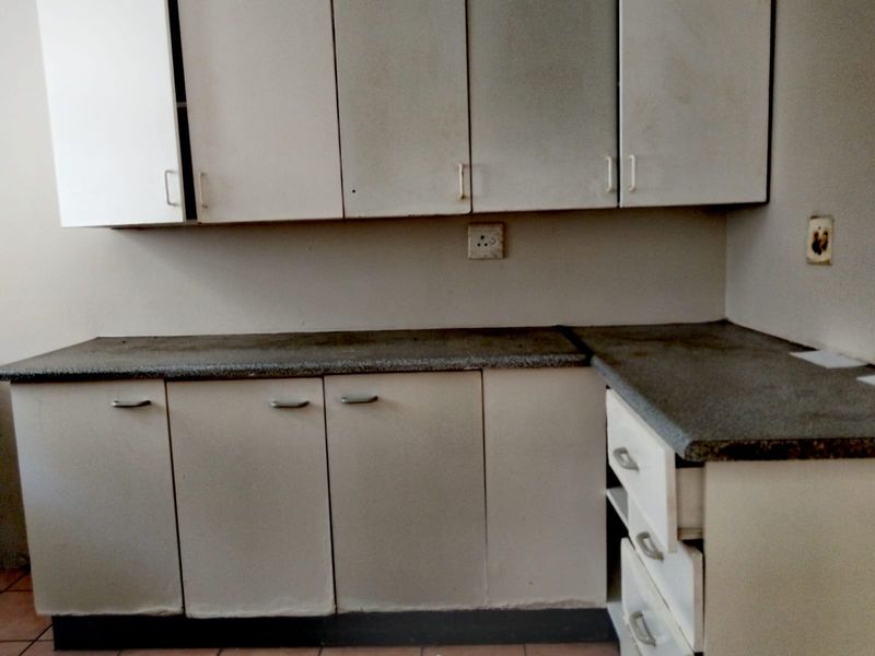 A dated kitchen area featuring built-in cabinetry, laminate countertops, and integrated drawer storage, requiring cosmetic updates to improve its overall aesthetic and functionality.