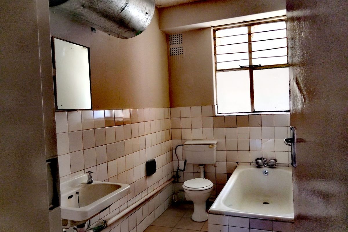 A dated bathroom featuring a wall-mounted basin, toilet, and bathtub with exposed plumbing and original tiling, requiring modernization and renovation.