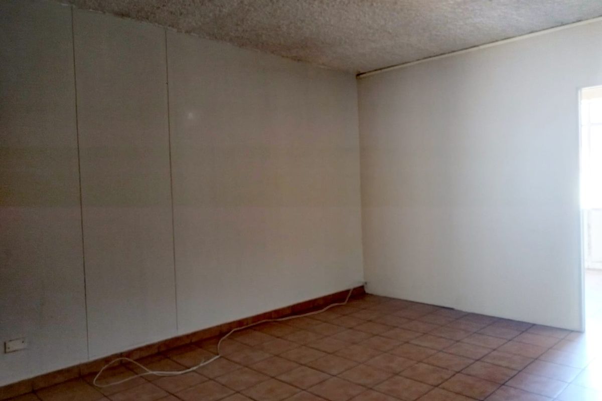 An empty living area featuring tiled flooring and a textured ceiling, offering a blank canvas for renovation and interior design updates.