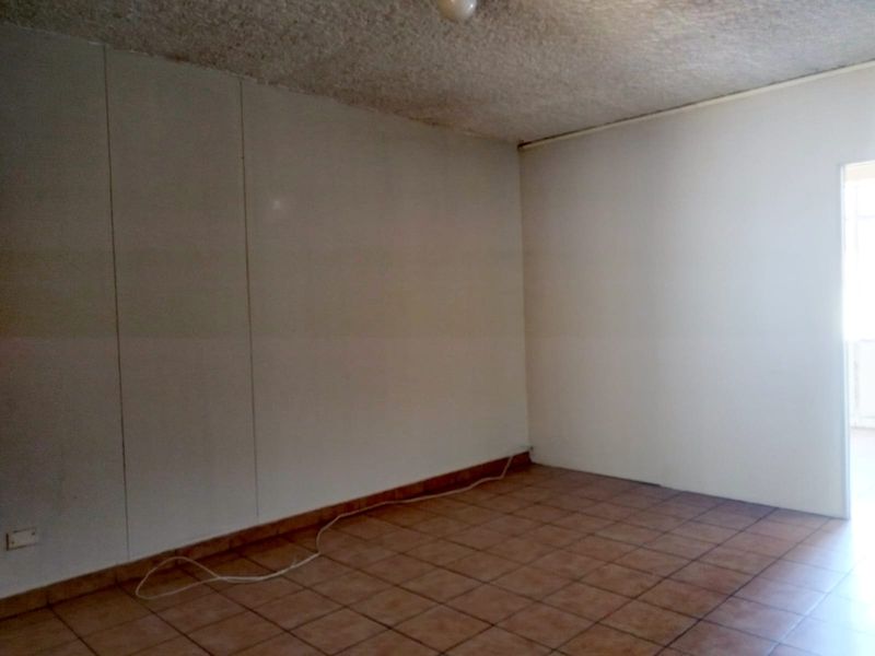 An empty living area featuring tiled flooring and a textured ceiling, offering a blank canvas for renovation and interior design updates.