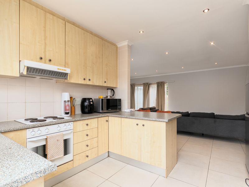 Open-plan kitchen featuring light wood cabinetry, laminate countertops, and integrated appliances, flowing seamlessly into the adjacent living area with tiled flooring throughout.