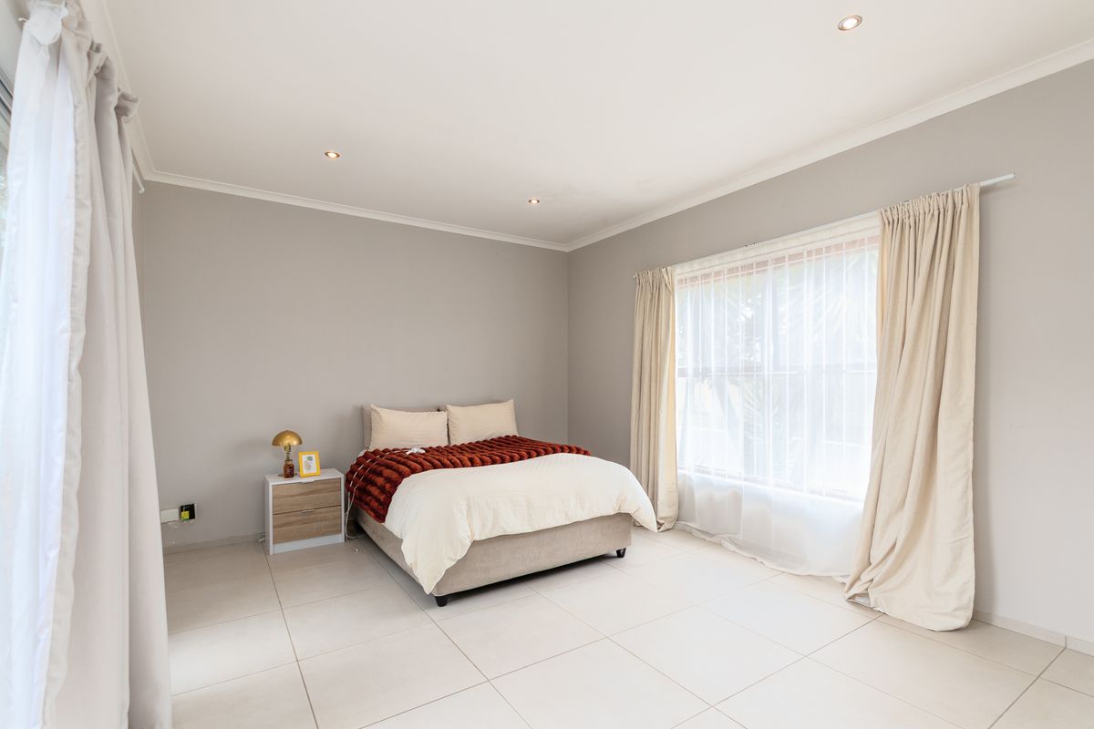 A bright and spacious bedroom featuring neutral wall tones, large windows with curtain tracks, and modern tiled flooring.