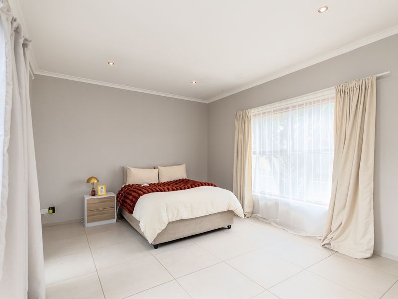 A bright and spacious bedroom featuring neutral wall tones, large windows with curtain tracks, and modern tiled flooring.