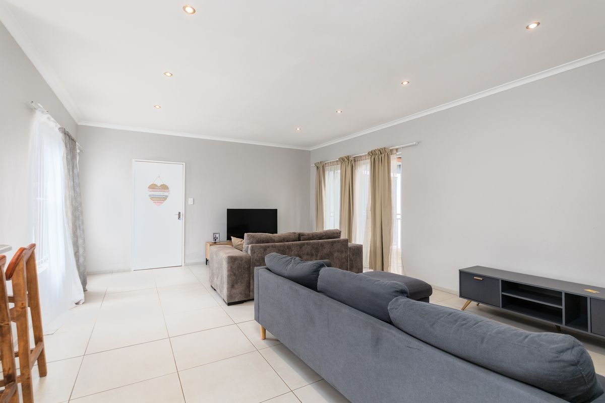 A bright and spacious living room featuring neutral tiled flooring, recessed downlighting, and large sliding glass doors that provide ample natural light.