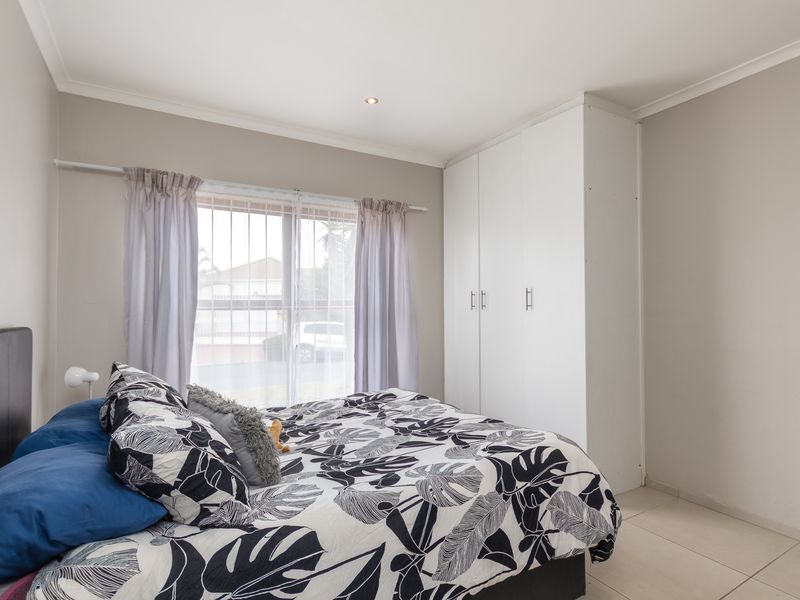 A well-maintained bedroom featuring neutral wall tones, tiled flooring, recessed lighting, and a functional white built-in wardrobe.