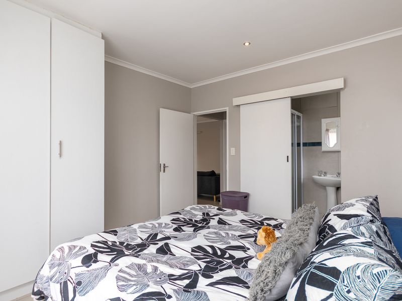A well-maintained bedroom featuring built-in cupboards and an en-suite bathroom with a pedestal basin and shower enclosure.
