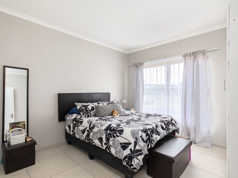 A well-maintained bedroom featuring neutral wall tones, tiled flooring, and large windows fitted with security bars and curtain rails.