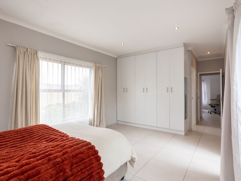 A bright and spacious bedroom featuring neutral tiled flooring, ample built-in cupboard storage, and recessed downlighting.