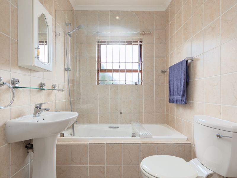 A functional bathroom featuring a pedestal basin, a built-in bathtub with a glass shower screen, and neutral wall tiling.