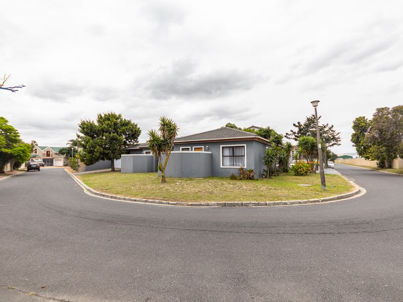 A corner-lot residential property featuring a grey rendered facade, tiled roof, and surrounding landscaped garden area situated on a quiet suburban street.