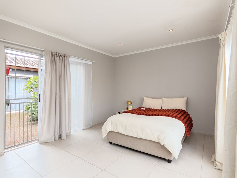 A bright and spacious bedroom featuring neutral tiled flooring, recessed downlighting, and a sliding glass door providing direct access to the exterior.