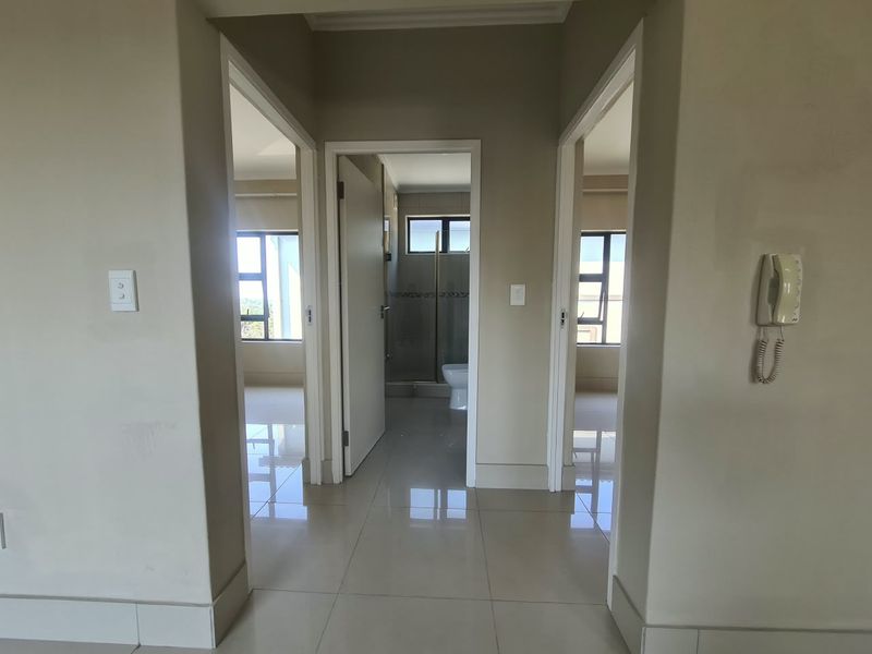 A bright, empty hallway featuring tiled flooring and an intercom system, providing access to multiple rooms within the apartment.