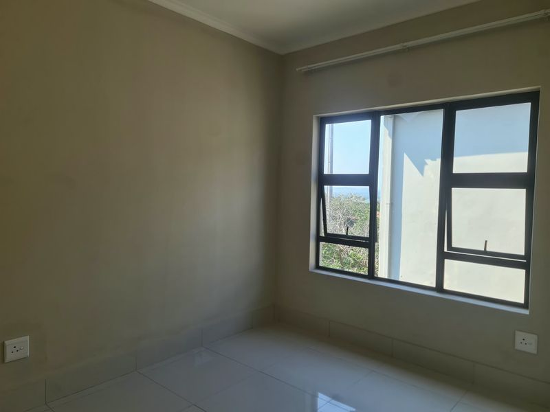 An empty bedroom featuring neutral wall paint, tiled flooring, and large aluminium-framed windows allowing for natural light.