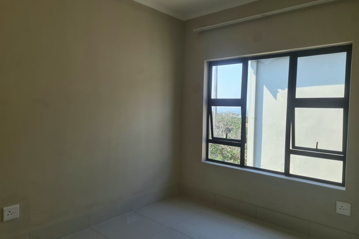 An empty bedroom featuring neutral wall paint, tiled flooring, and large aluminium-framed windows allowing for natural light.