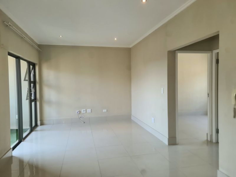 A bright and spacious empty living area featuring neutral tiled flooring, recessed downlighting, and a large sliding glass door leading to an outdoor space.