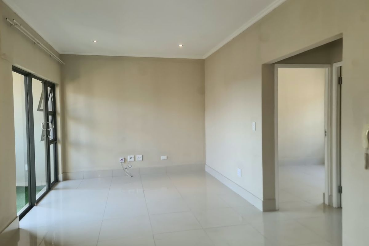 A bright and spacious empty living area featuring neutral tiled flooring, recessed downlighting, and a large sliding glass door leading to an outdoor space.