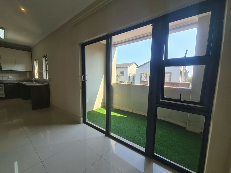 Open plan living area featuring tiled floors and sliding doors leading to a private balcony, adjacent to a modern kitchen with granite countertops.