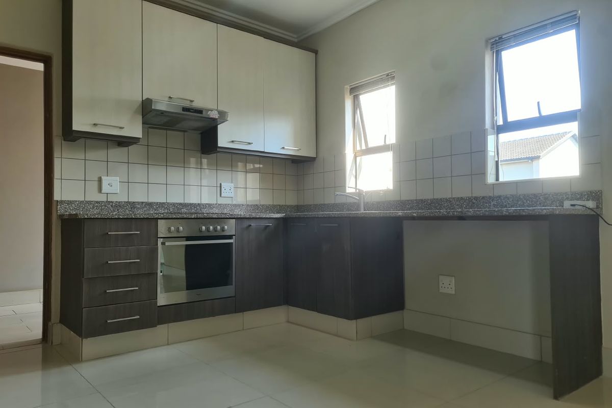A clean, modern kitchen featuring two-tone cabinetry, granite countertops, built-in oven with extractor fan, and ample natural light from dual windows.