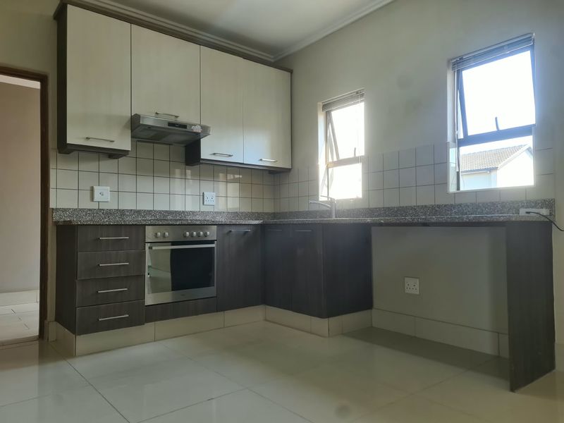 A clean, modern kitchen featuring two-tone cabinetry, granite countertops, built-in oven with extractor fan, and ample natural light from dual windows.