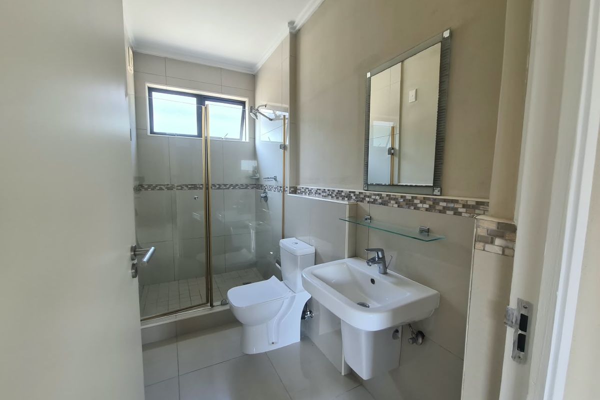 A clean and functional bathroom featuring a glass-enclosed shower, wall-mounted basin, toilet, and neutral tiled finishes throughout.