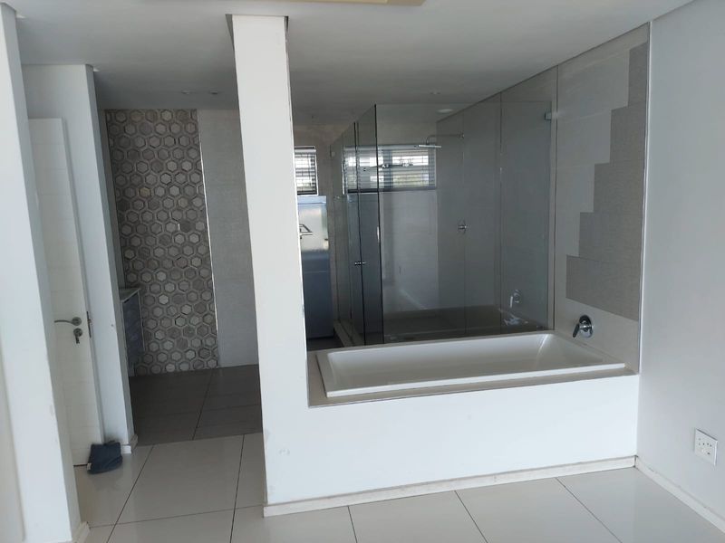 Modern open-plan bathroom featuring a built-in bathtub, glass-enclosed shower, and stylish hexagonal feature tiling.