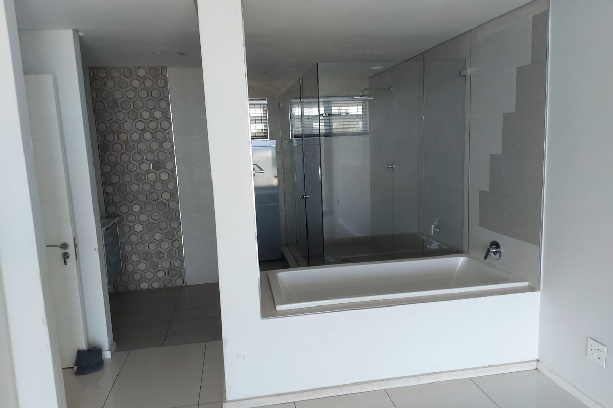 Modern open-plan bathroom featuring a built-in bathtub, glass-enclosed shower, and stylish hexagonal feature tiling.