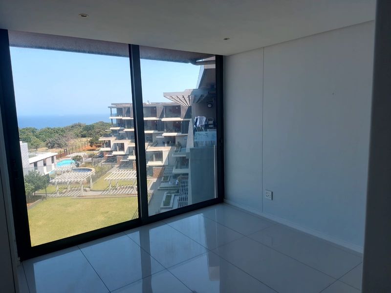 A bright, empty bedroom featuring large sliding glass doors that offer expansive views of the surrounding estate and ocean.