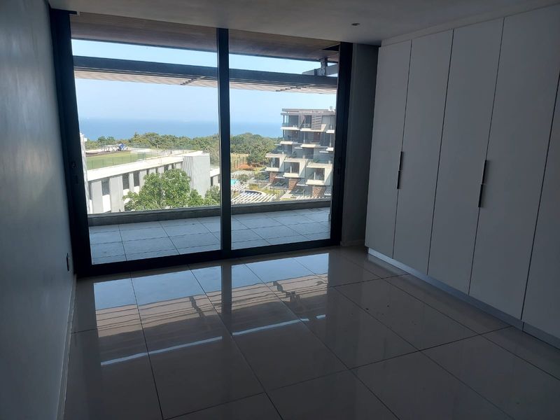 A bright, empty bedroom featuring modern built-in cupboards, large sliding glass doors, and access to a private balcony with scenic views.