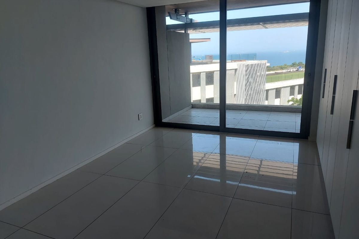 A bright, empty bedroom featuring modern tiled floors, built-in cupboards, and large sliding glass doors opening onto a balcony with ocean views.