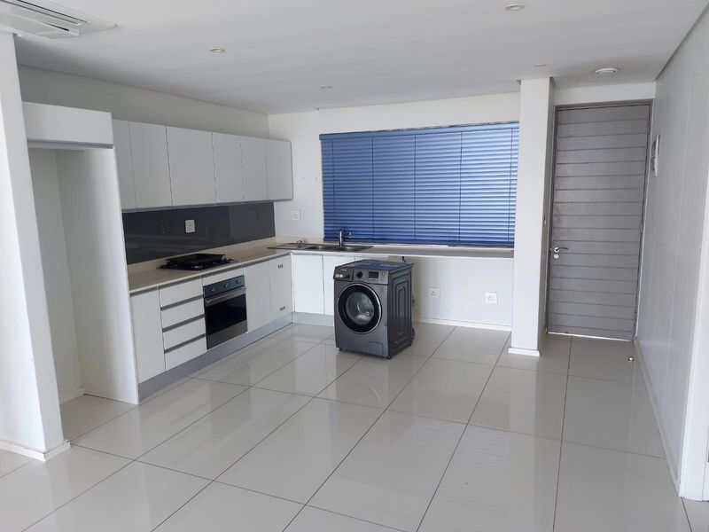 Modern kitchen featuring white cabinetry, integrated oven and hob, tiled flooring, and a neutral color palette, offering a clean and functional workspace.