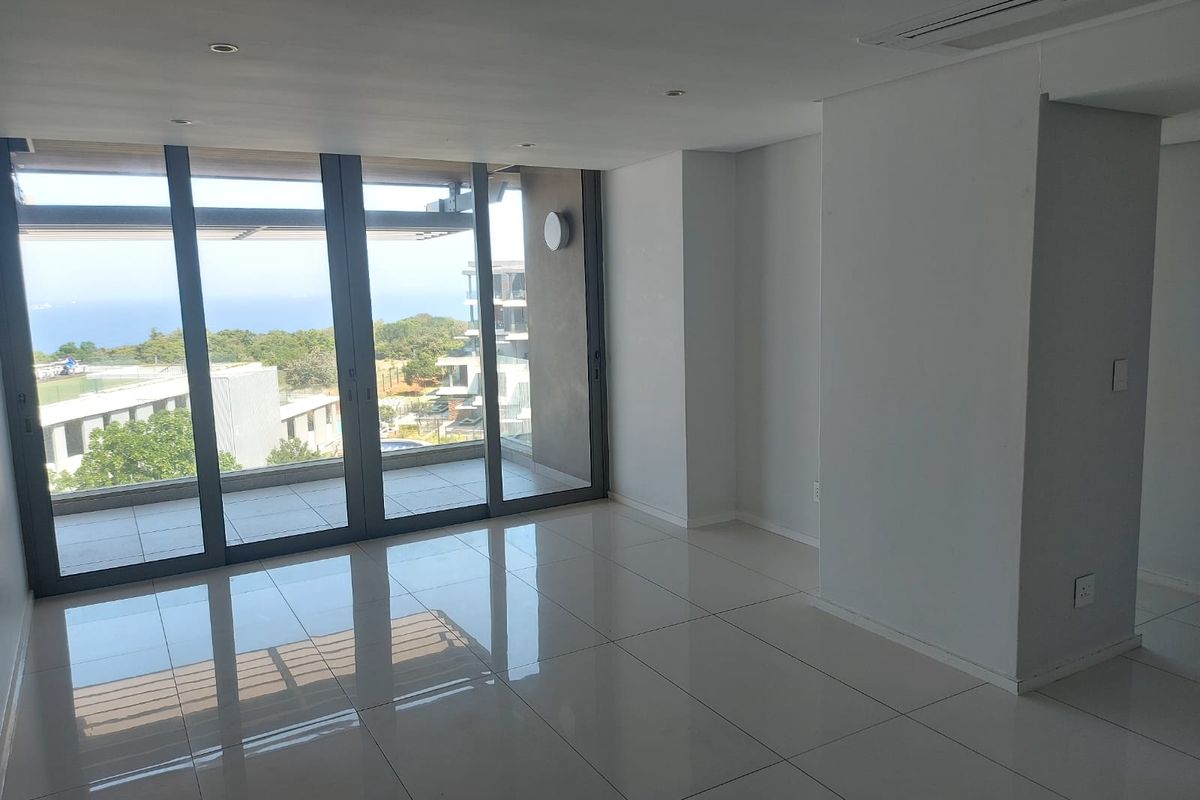 A bright, modern, and empty living area featuring large floor-to-ceiling sliding glass doors that open onto a balcony with scenic views.