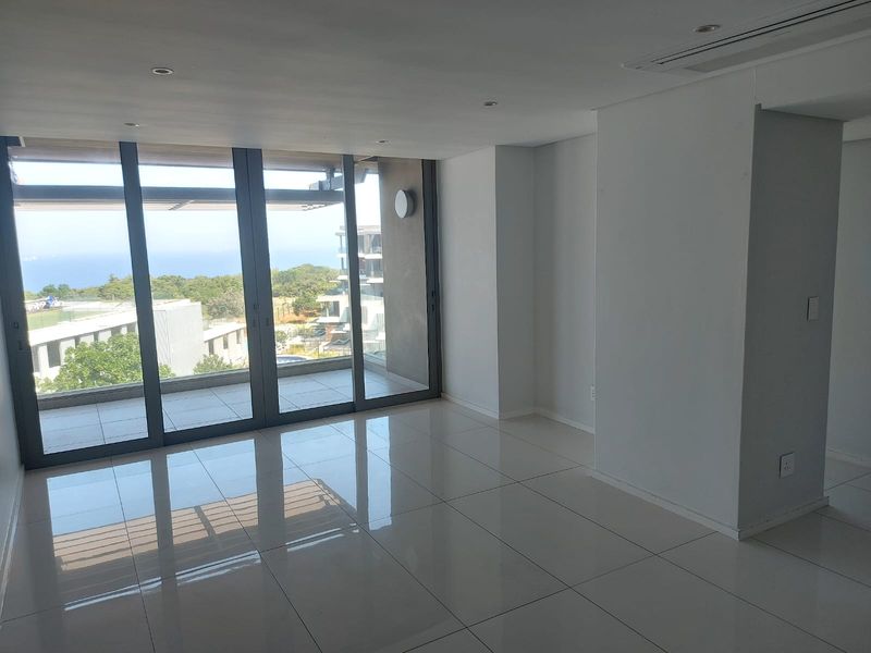 A bright, modern, and empty living area featuring large floor-to-ceiling sliding glass doors that open onto a balcony with scenic views.