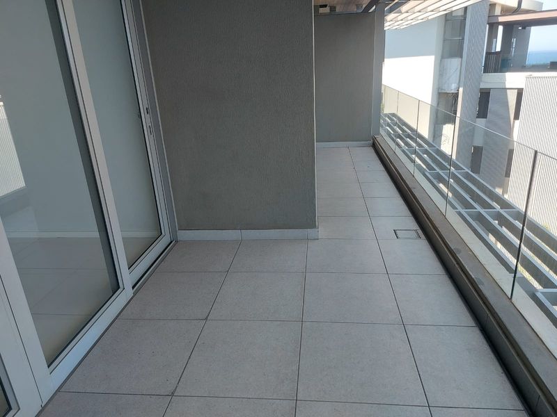 A modern, clean balcony featuring large format floor tiles, a sleek glass balustrade, and sliding door access to the interior.