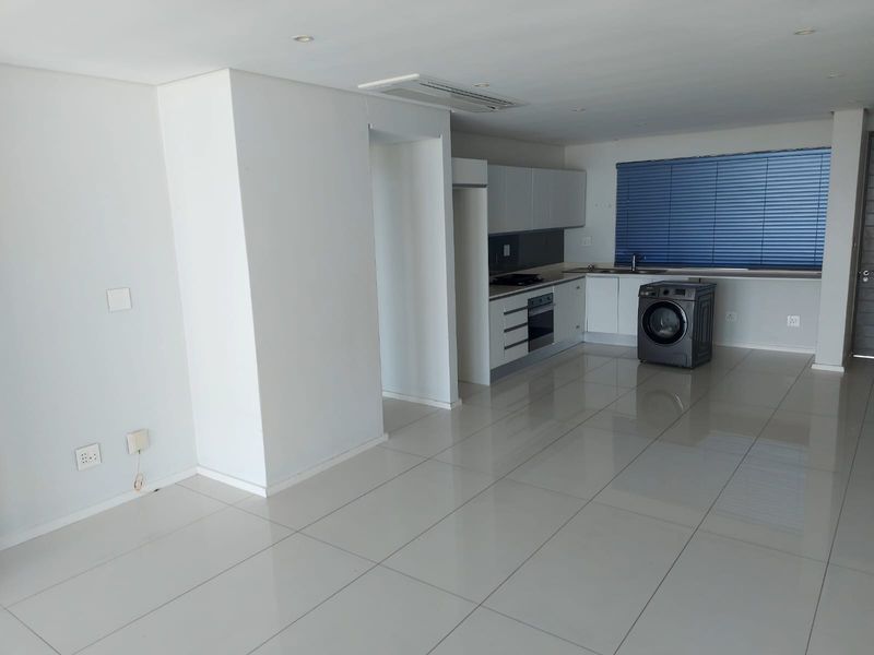Spacious open-plan kitchen and living area featuring modern cabinetry, integrated appliances, tiled flooring, and ducted air conditioning in a clean, neutral setting.