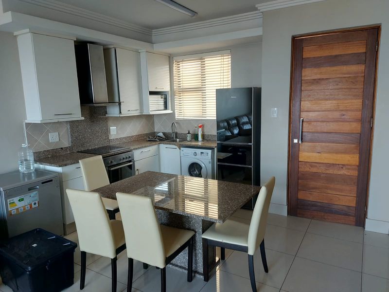 Open-plan kitchen and dining area featuring granite countertops, built-in cabinetry, integrated appliances, and tiled flooring with a solid wood entrance door.