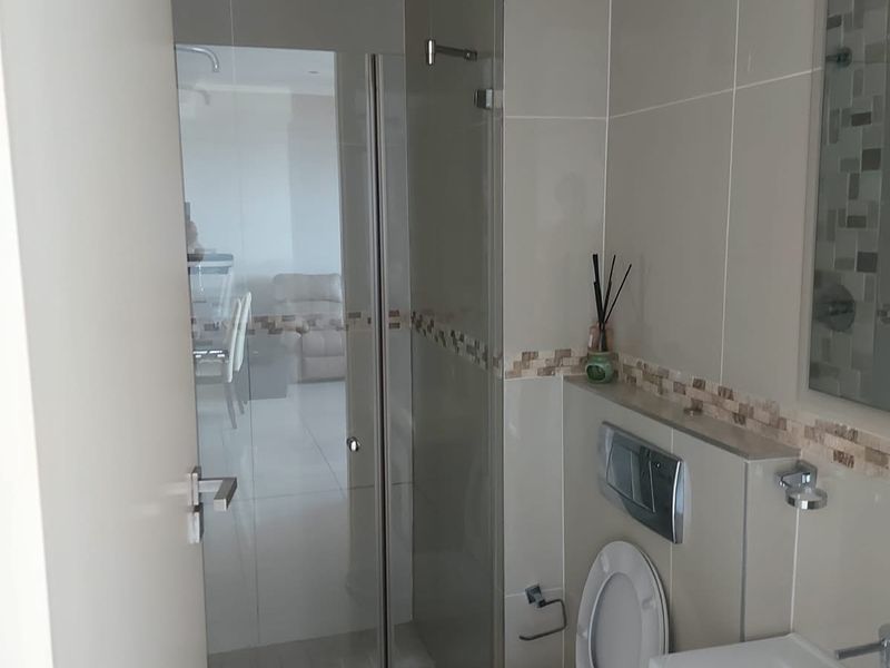 Modern bathroom featuring a wall-mounted toilet with concealed cistern, glass shower enclosure, and a vanity basin with neutral wall tiling.