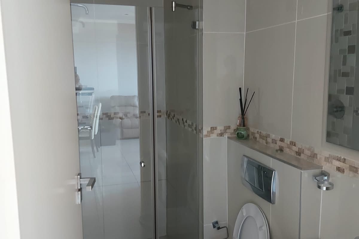 Modern bathroom featuring a wall-mounted toilet with concealed cistern, glass shower enclosure, and a vanity basin with neutral wall tiling.