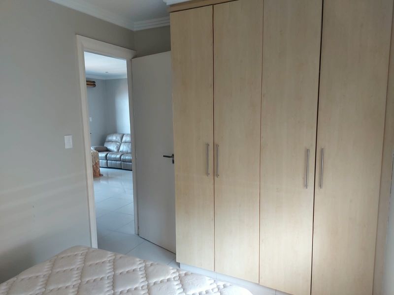 A bedroom featuring light wood-finish built-in cupboards and a doorway leading to an adjacent living area.