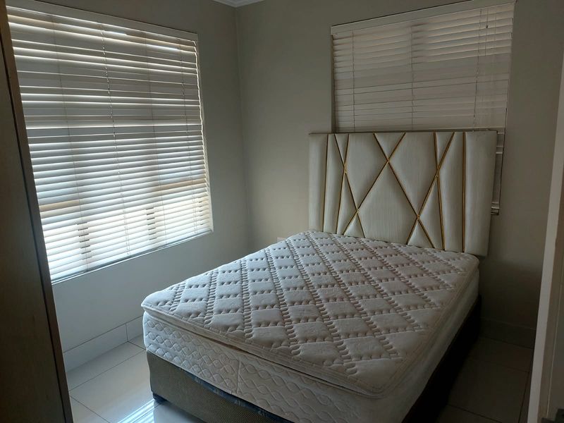 A well-lit bedroom featuring neutral wall tones, tiled flooring, and dual windows fitted with venetian blinds.
