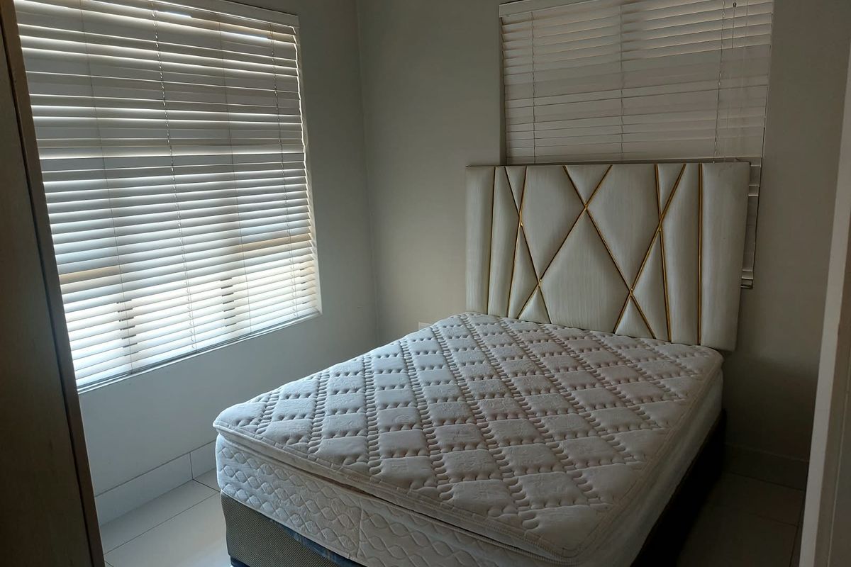 A well-lit bedroom featuring neutral wall tones, tiled flooring, and dual windows fitted with venetian blinds.