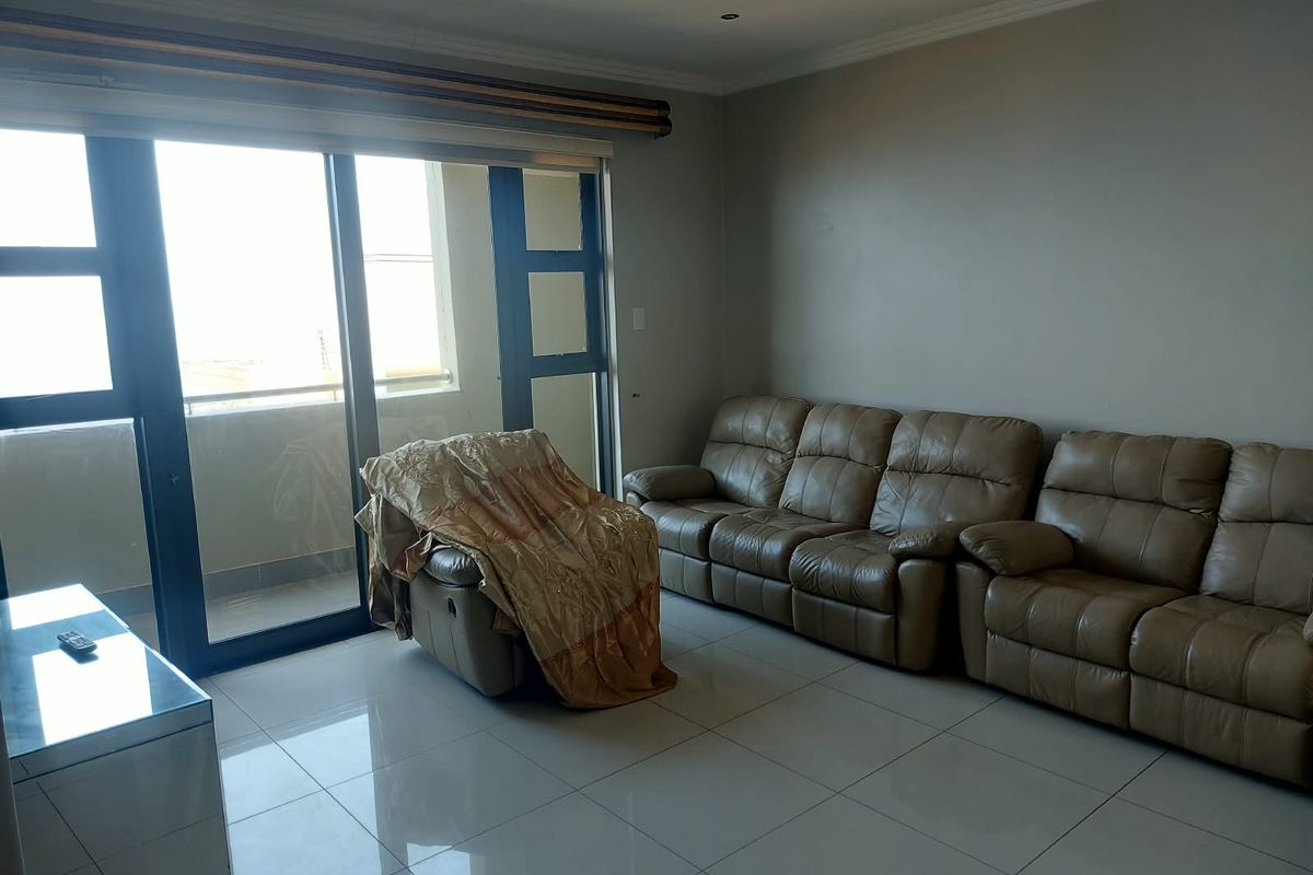 A living room featuring large sliding glass doors providing natural light, tiled flooring, and recessed ceiling lighting.