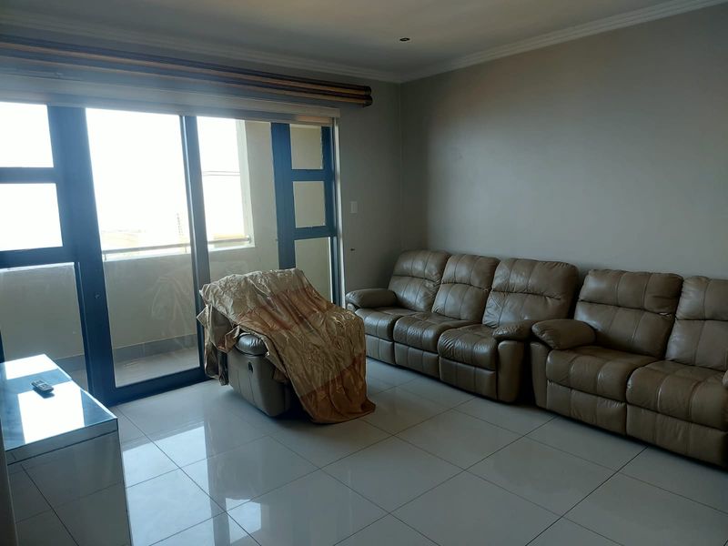 A living room featuring large sliding glass doors providing natural light, tiled flooring, and recessed ceiling lighting.