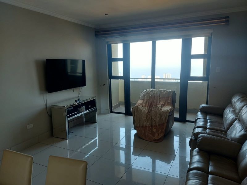 A bright living room featuring large sliding glass doors leading to a balcony, polished tiled flooring, and neutral wall finishes.