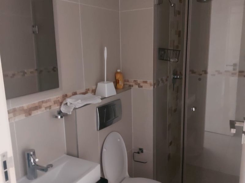 A functional bathroom featuring a wall-mounted toilet, a glass-enclosed shower, and a modern basin with a vanity unit.