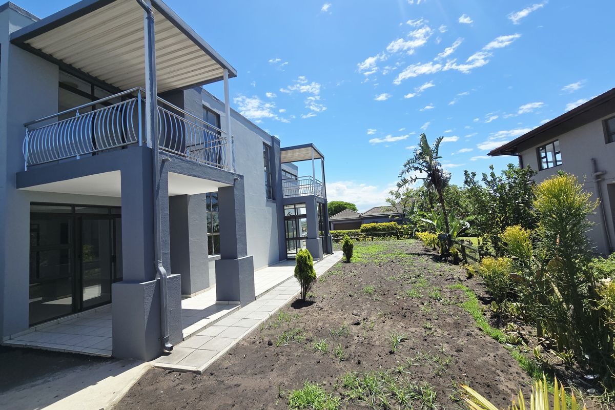Rear view of a modern double-story house featuring covered patios, balconies with metal railings, and a landscaped garden area.