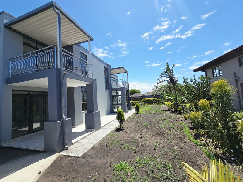 Rear view of a modern double-story house featuring covered patios, balconies with metal railings, and a landscaped garden area.