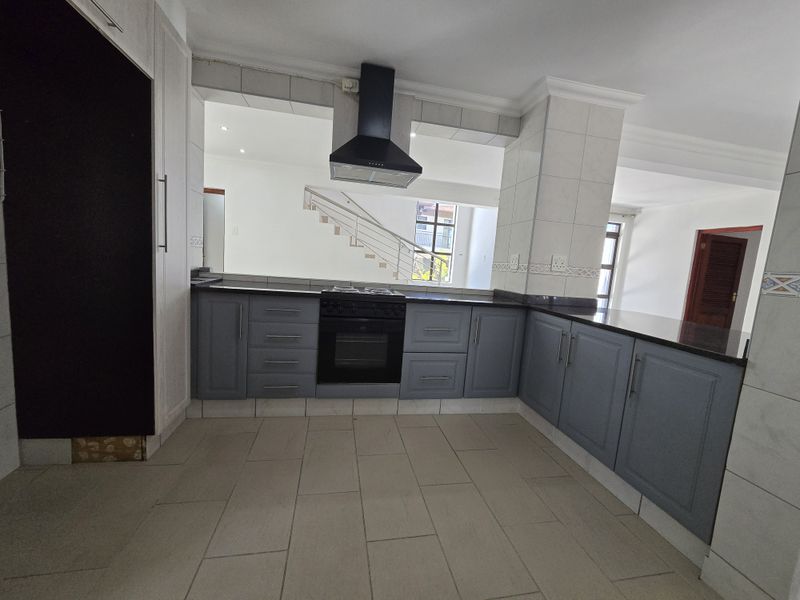 A spacious kitchen featuring grey built-in cabinetry, granite countertops, a built-in oven with hob, and an extractor fan, with an open-plan layout.