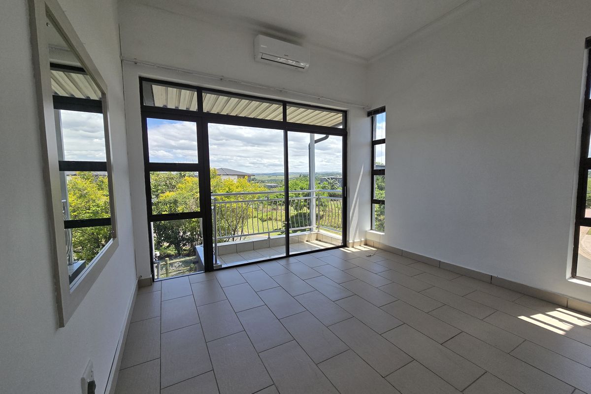 A bright, empty living area featuring tiled floors, a wall-mounted air conditioner, and large sliding glass doors opening onto a balcony with scenic views.