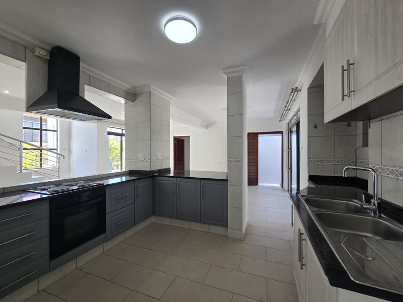 A modern, spacious kitchen featuring dark grey cabinetry, granite countertops, built-in oven and hob, and tiled flooring in an open-plan layout.
