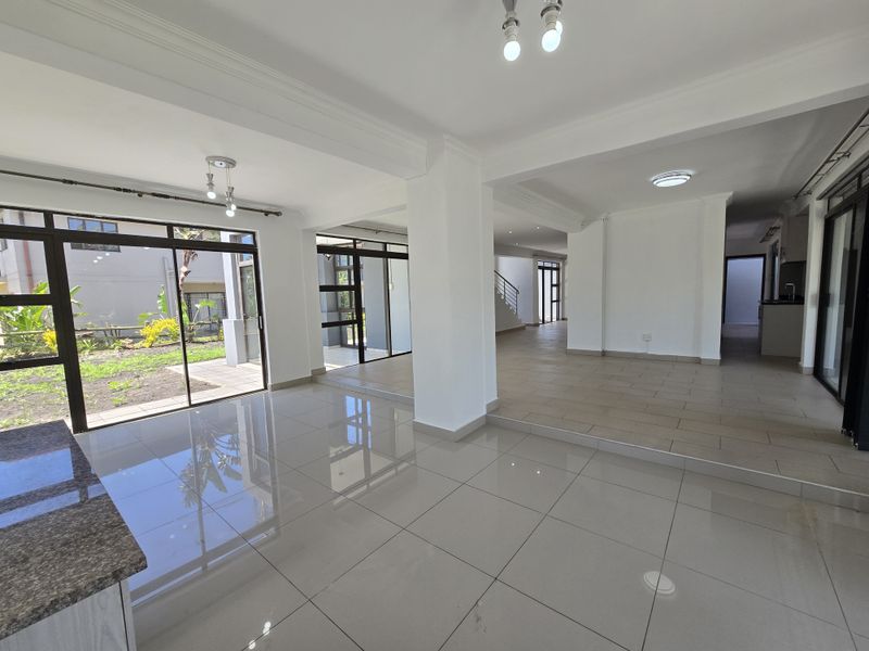 Spacious open-plan living area featuring large format porcelain tiles, abundant natural light through sliding glass doors, and a seamless flow to the outdoor garden.